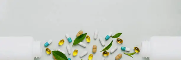Photo of Different tablets, capsules, pills are scattered from the jar on a light background The concept of health Minimalism