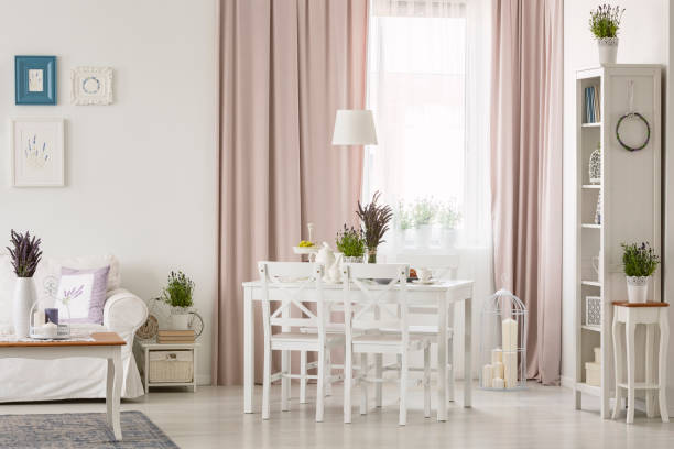 istock Lamp above table and chairs in white and pink apartment interior with posters and drapes. Real photo 1036660832
