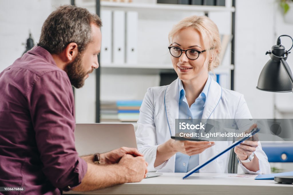 patient having appointment with smiling physiotherapist in hospital Doctor Stock Photo