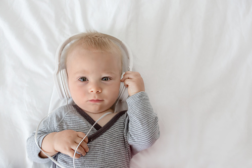 Cute little toddler baby boy listening music with head phones in bed