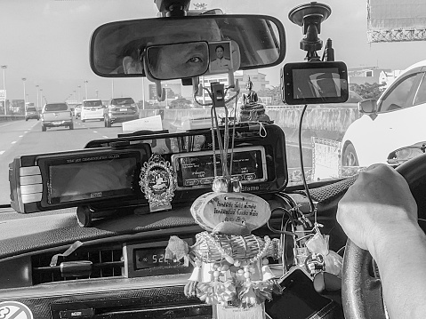 Inside a Thai taxi the Taxi driver prepares many to pay at an expressway toll booth in the heart of Bangkok city, many traditional and religious good luck charms and traditional paraphernalia are on display on the dashboard.