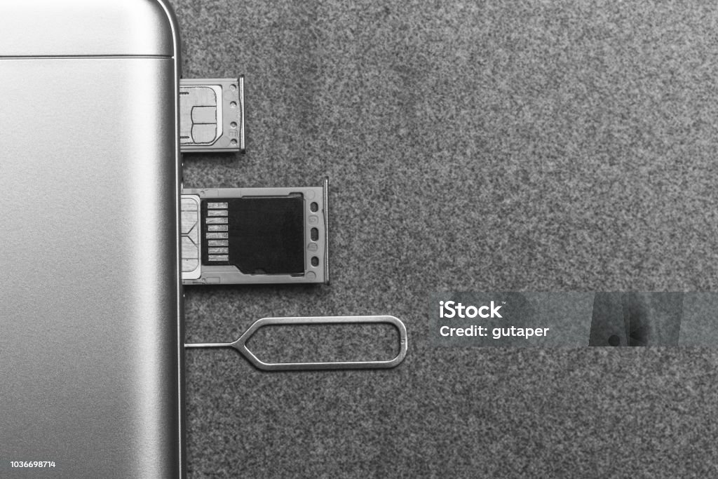 mobile phone and open slots for nano SIM cards, micro SD drive and metal key on grey background with copy space, black and white photo Backgrounds Stock Photo
