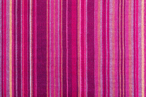 Striped fabric texture with multiple warm colors (purple, purple, magenta, pink, red, maroon, orange, yellow). Close-up of the tissue. Ethnic aspect