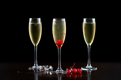 Elegant composition with three nice high crystal cocktails glasses with transparent cold drink, melting ice cubes and ripe red cherries on shiny dark surface on deep black copy space background.