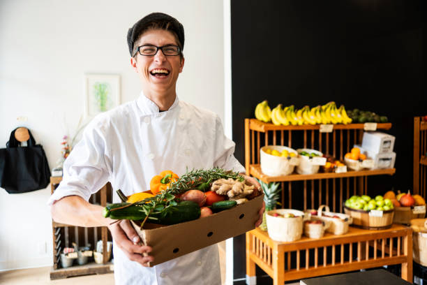 jeune chef avec une boîte pleine de produits d’épicerie bio - grocer photos et images de collection