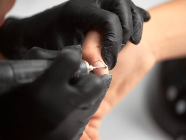 istock Close-up of professional beautician hands working with electric drill file on client fingernails. 1036731004