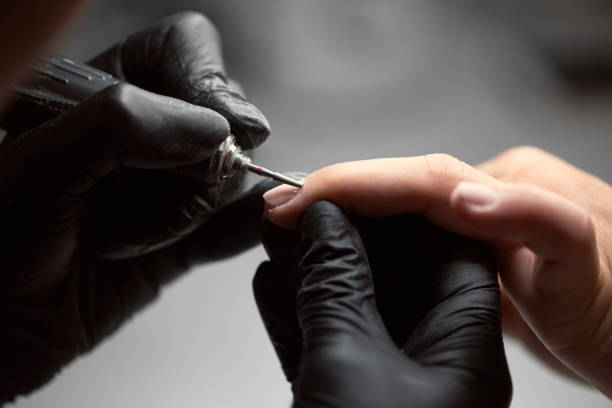 istock Close-up of professional beautician hands working with electric drill file on client fingernails. 1036731498