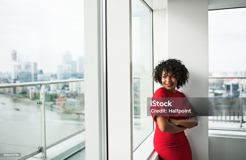 A portrait of woman standing by the window against London view panorama. A portrait of woman standing by the window against London rooftop view panorama. Copy space. Looking Through Window Stock Photo
