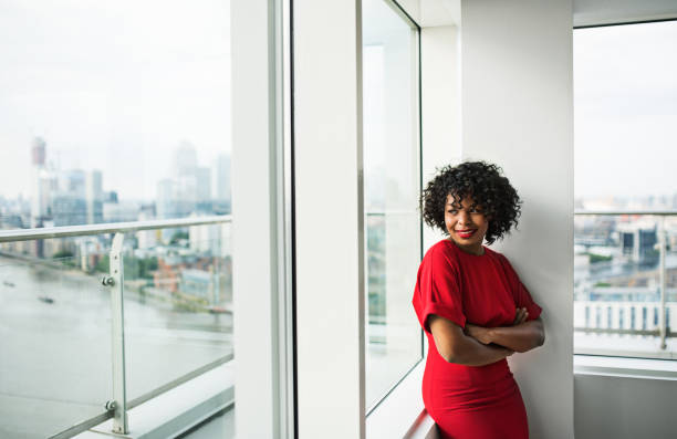 A portrait of woman standing by the window against London view panorama. A portrait of woman standing by the window against London rooftop view panorama. Copy space. woman in red dress stock pictures, royalty-free photos & images