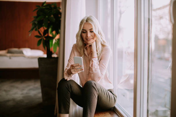 istock Pretty young woman with mobile phone by the window 1036740188