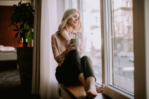 istock Blonde young woman drinking coffee by window 1036740200