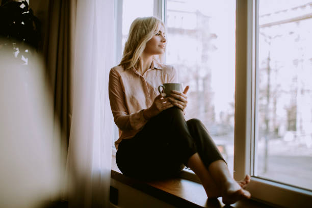 istock Blonde young woman drinking coffee by window 1036740210