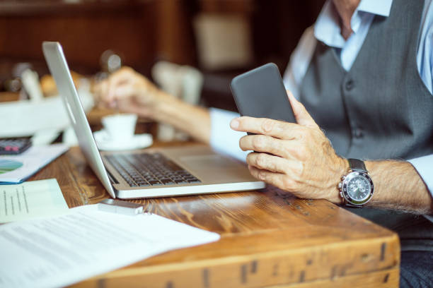 Businessman holding mobile phone and stirring coffee Unrecognizable senior male person in coffee shop stirring coffee drink and holding mobile smart phone. There are laptop computer and paper files on the table. stirring stock pictures, royalty-free photos & images