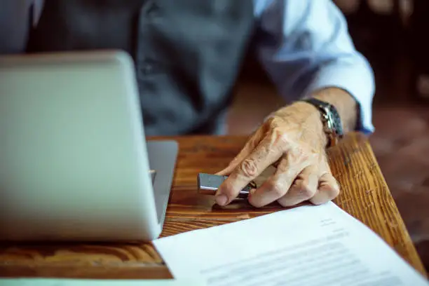 Unrecognizable senior male person using USB device on laptop computer in co-working space.