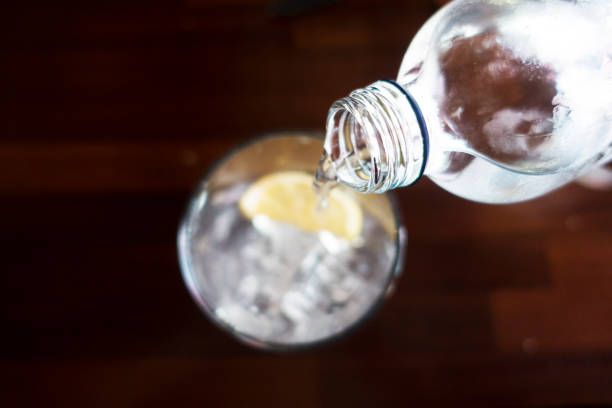 gießt wasser aus der flasche ins glas auf hölzernen hintergrund - destilliertes wasser stock-fotos und bilder