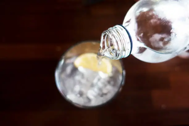 Pouring water from bottle into glass on wooden background