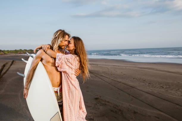 istock surfer hugging girlfriend and holding surfboard on beach in bali, indonesia 1036748740