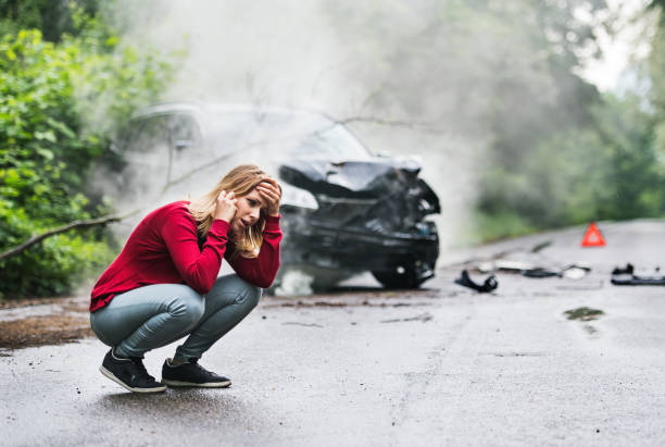 eine junge frau mit smartphone durch das beschädigte auto nach einem autounfall einen anruf tätigen. - mobile phone telephone frustration women stock-fotos und bilder