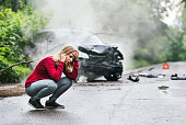A young woman with smartphone by the damaged car after a car accident, making a phone call.
