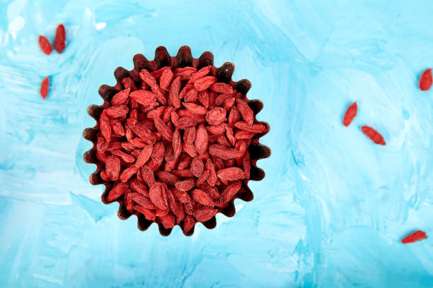 goji de súper alimentos en un recipiente pequeño sobre fondo azul. - quinoa sesame chia flax seed fotografías e imágenes de stock