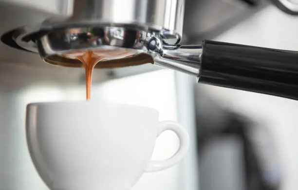 Barista using coffeemaker extraction for espresso shot in cafe.