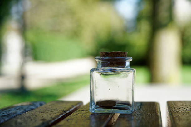 bouteille avec des pièces se trouve sur un banc de parc, bocal transparent - transparent ideas lid glass photos et images de collection