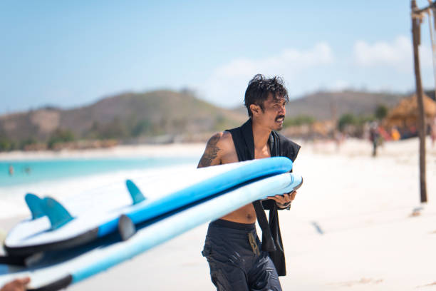 istock Indonesian man carrying surfboard on the beach 1036799428