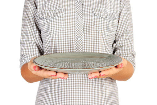 girl in the plaid shirt is holding an empty round green plate in front of her. woman hand hold empty dish for you design. perspective view, isolated on white background.