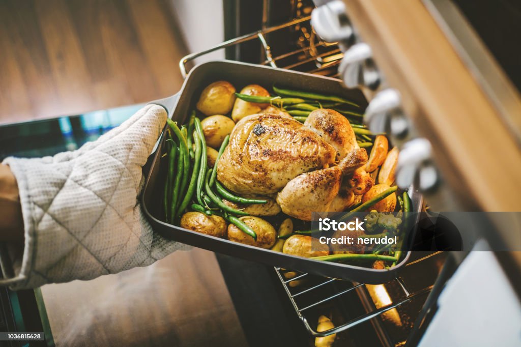 Cook taking ready chicken from the oven Cook taking ready fried baked chicken with vegetables from the oven. Healthy cooking concept. Cooking Stock Photo