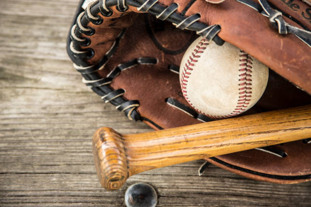 Baseball season is here.  Bat, glove and ball on dugout bench. Spring and summer baseball season is here.  Wooden bat, glove, and weathered ball lying on dugout bench in late afternoon sun.  No people.  Great background image. baseball baseballs spring training professional sport stock pictures, royalty-free photos & images