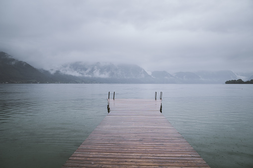 Silent morning in Traunkirchen. Wooden bridge on a lake. Mountains in clouds on the background.