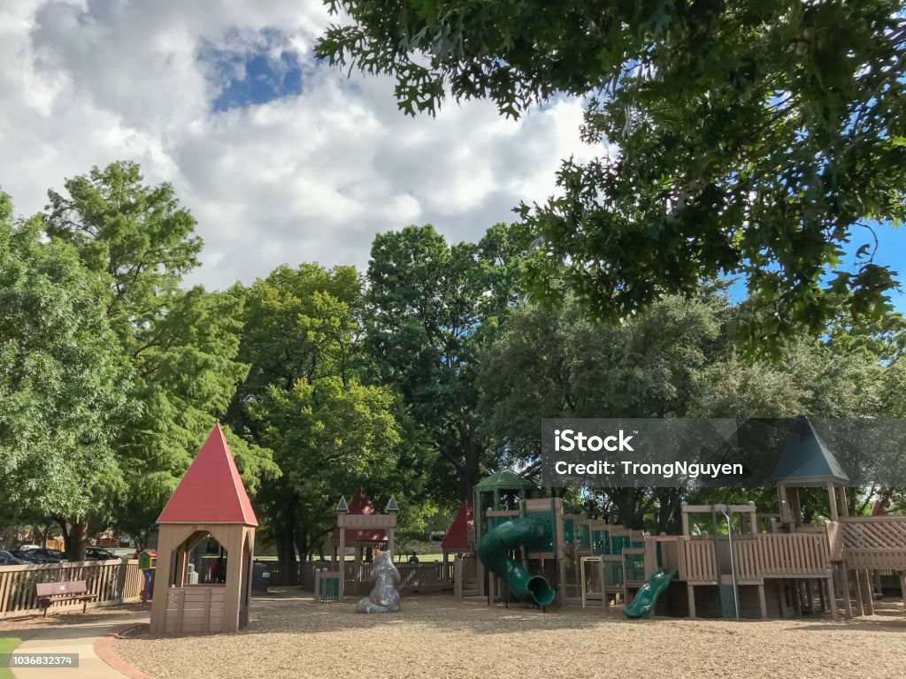 Public wooden castle style children playground in Coppell, Texas, USA Public wooden children playground like fort or castle with separate sections for different ages. Play set structure under the lush of larger trees in Texas, USA, summer leaves green and cloud blue sky Childhood Stock Photo