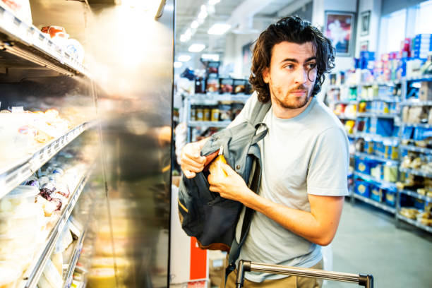 Un taccheggiatore maschio che ruba del costoso formaggio gourmet in un supermercato - foto stock