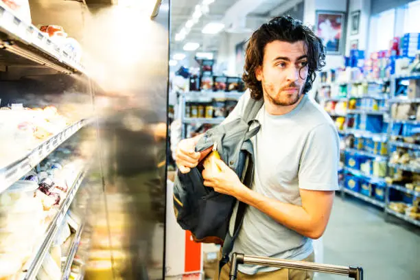 Photo of A male shoplifter stealing some expensive gourmet cheese in a supermarket