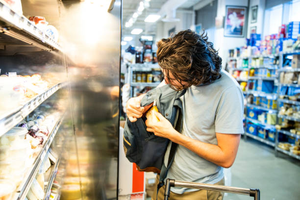 Un taccheggiatore maschio che ruba del costoso formaggio gourmet in un supermercato - foto stock