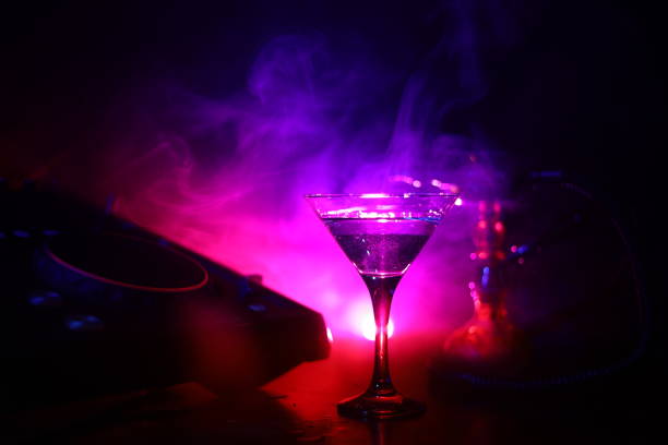 istock Glass with martini with olive inside on dj controller in night club. Dj Console with club drink at music party in nightclub with disco lights. 1036864662