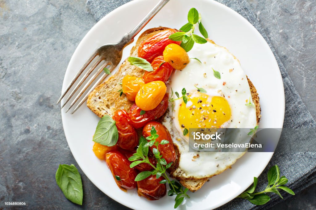 Multigrain toast with fried egg and roasted tomatoes Multigrain toast with fried egg, fresh herbs and roasted tomatoes Egg - Food Stock Photo