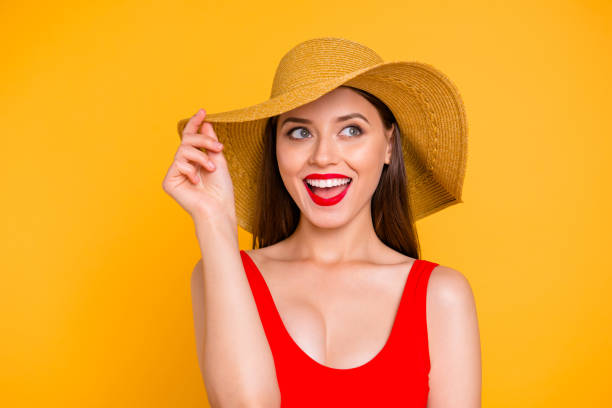 ビーチの時間!少女の肖像画に近い笑いと黄色の背景に分離された側の探している片方の手で帽子を保持してください。 - women summer hat beach ストックフォトと画像