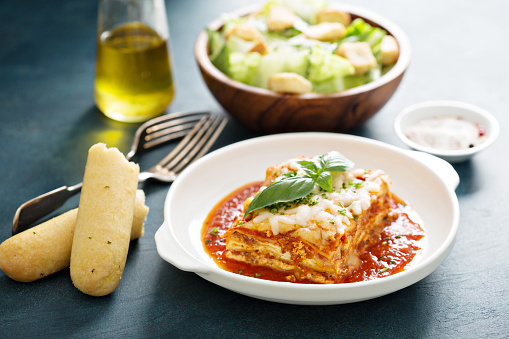Traditional lasagna on white plate with caesar salad and breadsticks