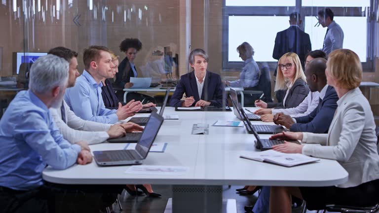 Wide dolly shot of a Caucasian business woman with shorter hair leading a meeting in the glass conference room. Shot in Slovenia.