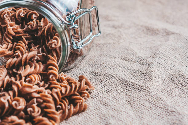 istock Raw Italian pasta in a glass jar on linen in the kitchen - horizontal format - close up - copy space 1036965946