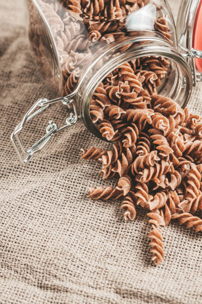 istock Raw Italian pasta in a glass jar on linen in the kitchen - vertical format - close up - copy space 1036970170