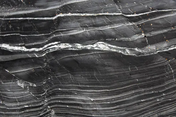 A geology background of layers of grey slate and marble compacted together in a cross section of a cliff side with copy space