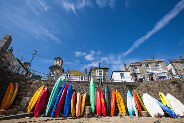 Mousehole, Cornwall, UK - September 5, 2018.  Colourful kayaks, canoes and surf boards standing upright on the sandy beach of the picturesque fishing village of Mousehole in Cornwall, UK which is a popular tourist destination.