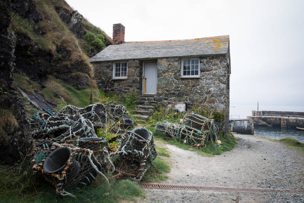 Mullion Cove, Cornwall, UK - September 3, 2018.  An old, stone, fisherman’s cottage or cellar with lobster pots on the ancient harbour of Mullion Cove in Cornwall which is a popular tourist destination.