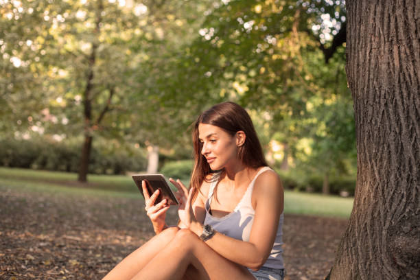 istock Woman reading tablet and enjoy rest in a park under tree . 1037008784