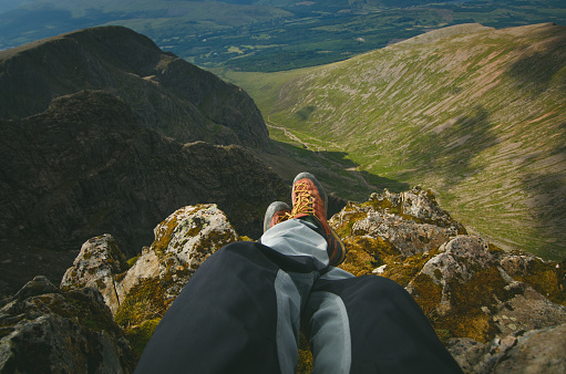 Man hiker sitting on the top of mountain rocks. Beautiful weather with Scotland nature.
 Detail of hiking boots on the difficult pathway, trail, Friends in the nature and enjoying sport.