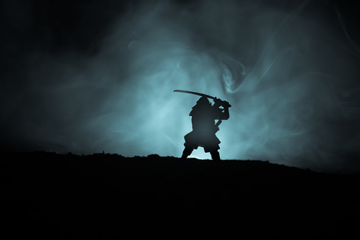 Fighter with a sword silhouette a sky ninja. Samurai on top of mountain with dark toned foggy background. Selective focus