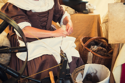 Cropped image of weaver in Middle Agesl clothes make yarn on spinning wheel. Medieval crafts, occupation. The concept of historical development of weaving in England. Selective focus. Copy space