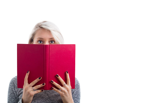 Portrait of a pretty young girl hiding behind an open red book and looking scared to camera isolated over white background.